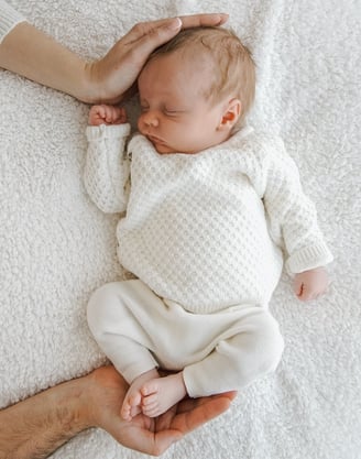 a baby is sleeping on a blanket and a man is holding his hands up to