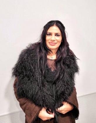 Raquel Alves posing for the camera with a brown furred coat and a smile.