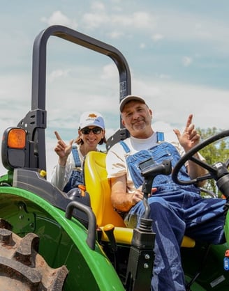 Dr. Norwood on a John Deere tractor giving the "Go Pokes!" sign.