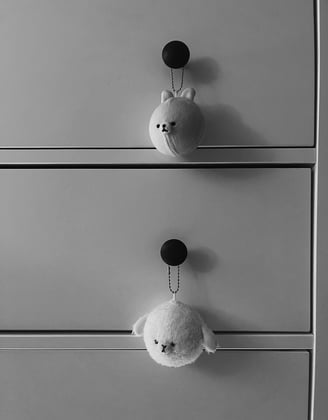 two stuffed toy keychains from the brand Mofmo Friends are hanging on the knobs of a dresser