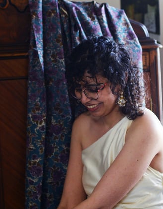 a curly-haired woman in a white dress looks away from the camera.