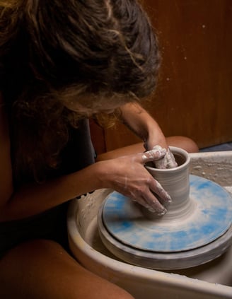 A person leaning over a piece while throwing on a potter's wheel.