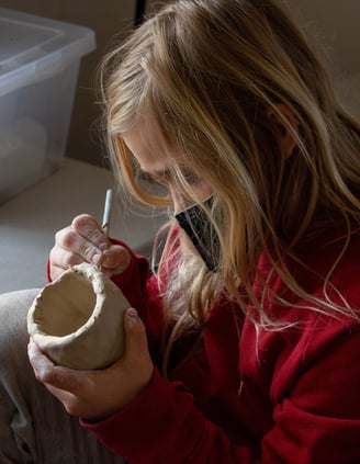 Young girl using a pencil tool to carve into a small ceramic cup.