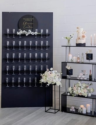 Black champagne wall with champagne flutes white floral. This set up was featured on wedluxe 