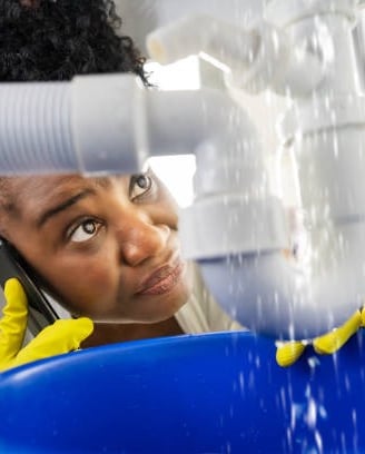 woman on the phone staring at her leaking pipe