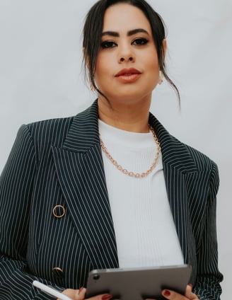 a woman in a suit and necklaces holding a tablet