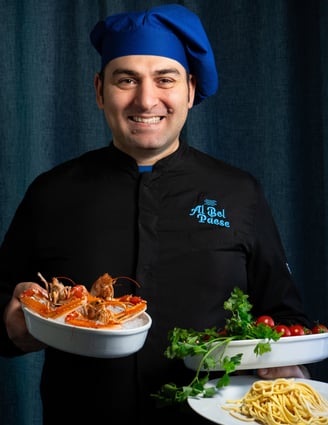 Chef Vito Amodio che presenta ingredienti freschi per la cucina: scampi, pasta fresca e pomodori