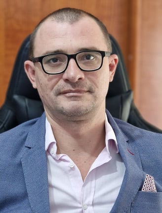 a man in a suit and glasses sitting in a chair smilling