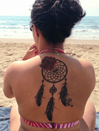 Femme de dos sur la plage, tatouage de rose et capteur de rêves, symbole de mémoire et lignée spirit