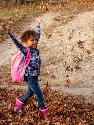 Young girl walking to Access Arts throwing leaves in the air.