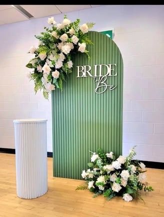 green bridal shower backdrop with a bride to be sign and floral arrangement