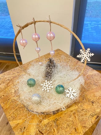 Decor de iarnă cu globuri roz și verzi, fulgi albi și con de brad, pe bază rustică din lemn.