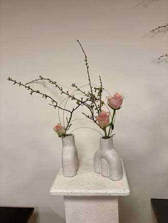 Ikebana modernă cu trandafiri roz și crenguțe, în vaze ceramice albe.