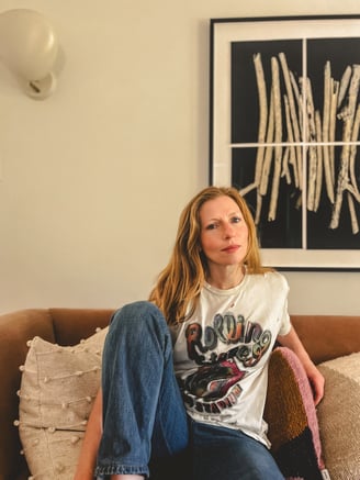 Editorial portrait of a yoga teacher with red hair and somatic practitioner, seated on a sofa. 