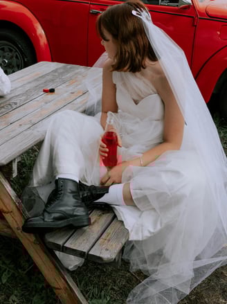a young women on her wedding day, dressed in funky doctor martins witha red bettle car behind her