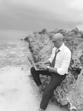 « Bruno Valery travaillant sur son ordinateur, assis sur un rocher les pieds dans l’eau en Guadeloupe »