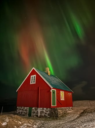 "Red house in the snowy Faroe Islands under vibrant northern lights in green, red, and orange hues."