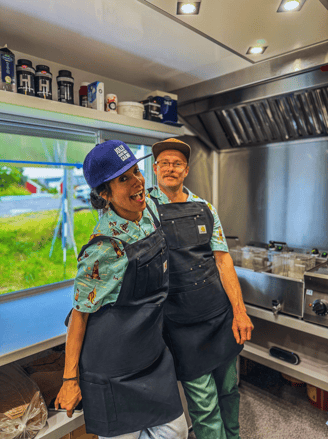 a man and woman in aprons inside the top rated fish and chips food truck located in Hamnøy, Lofoten