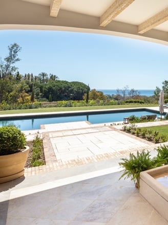 View from the shaded porch across the pool, with the Mediterranean Sea visible in the background.