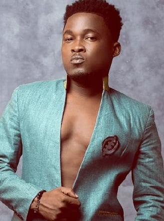 Bless posed in a green shirt with an Adinkra symbol.