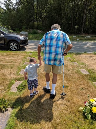 An older man with a cane walks with a small child at a cemetary