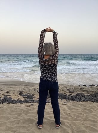 a woman standing on a beach with her arms up in the air