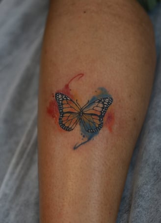 Butterfly tattoo with red and blue watercolor fill on leg by Dudo’s Hyderabad