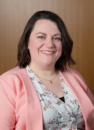 a woman in a pink jacket and a floral shirt with cross necklace