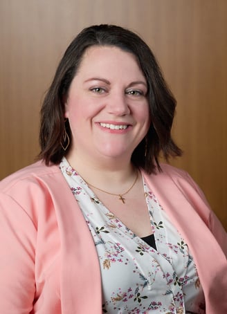 a woman in a pink jacket and a floral shirt with cross necklace