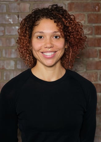 El, a Black bi-racial nonbinary psychotherapist with curly hair smiles into the camera