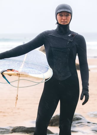 A female surfer wearing full winter kit holding a longbaord at the beach