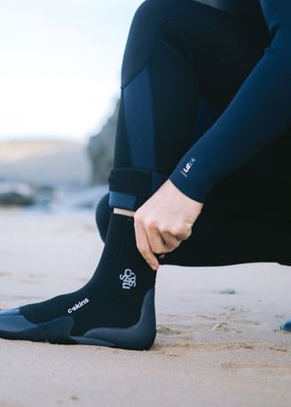 A man pulling on a wetsuit boot at the beach