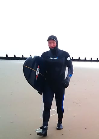 A male surfer walking up Ynyslas beach in full winter setsuit gear