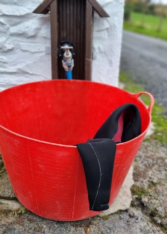 A wetsuit in a red bucket about to be rinsed