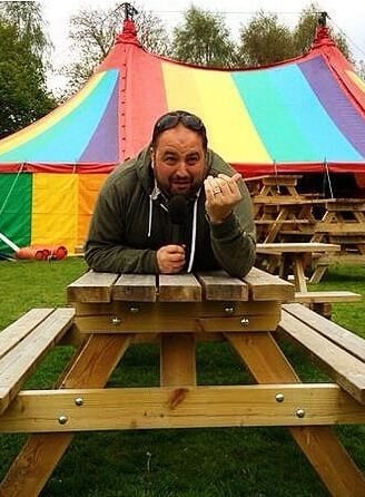 Wynne Evans lying on a picnic beach with a colourful circus tent in the background