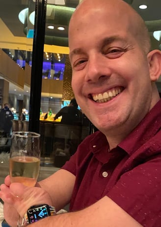Yoav Rokach Penn wearing a red dress shirt, in a restaurant holding a Champaign glass.