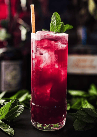 a glass of alcohol with a strawberries and mint leaves