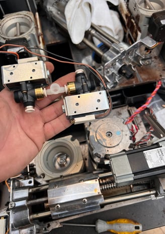 Close-up of solenoid valves removed for replacement during Mastrena 2 espresso machine maintenance.