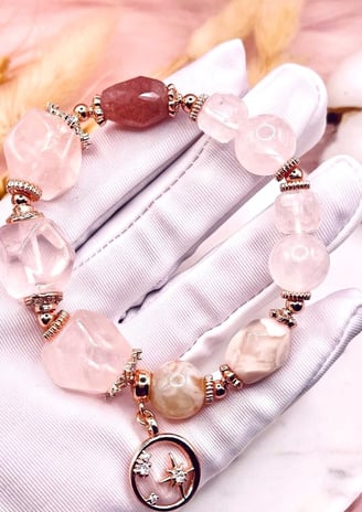 A gloved hand holding a delicate crystal bracelet with pink and translucent gemstones, along with si