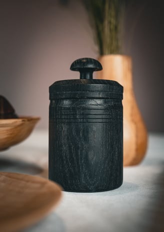 Pot à épices en bois foncé artisanal avec couvercle sculpté, posé sur une table. Sa texture naturell