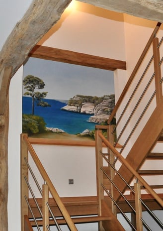 Une ouverture en trompe-l'oeil dans une cage d'escalier, invite au voyage en bord de mer. Le faux bois intègre l'ensemble.