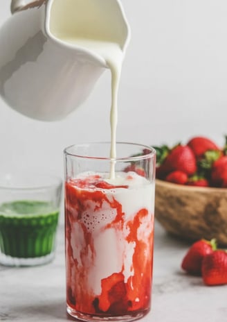 Milk being poured over strawberry layer in iced glass