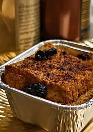 A crispy bread and butter pudding for sugar or gluten free, with a steady stream of crème anglaise being poured over it.