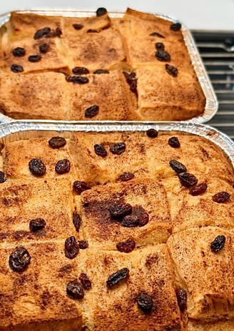 Crisp bread and butter pudding served in big tray with crème anglaise being poured in a steady stream over it