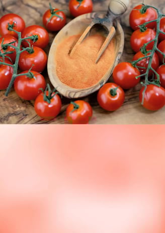 Bright red tomato powder in a wooden bowl with fresh tomatoes in the background
