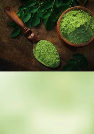 Green moringa powder in a ceramic bowl with fresh moringa leaves nearby