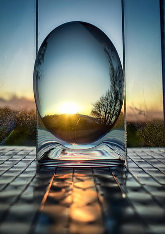 An AI generated image of a transparent glassy egg in front of a window at sunset