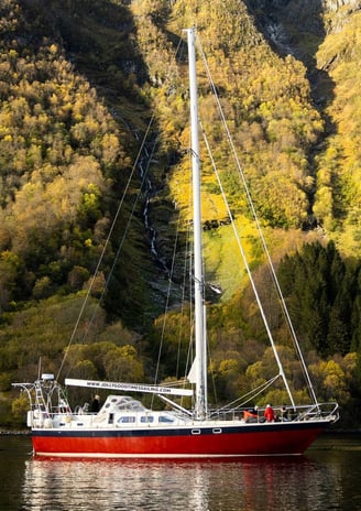 a sailboat in Norway in the water with a waterfall in the background | Sailing adventures in Norway 