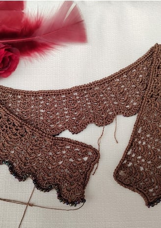 Collier au crochet dans un fil de soie marron dans un point fantaisie sur le haut gauche des plumes