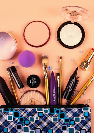 oranje achtergrond met op de voorgrond penselen , kwasten, lippenstift, blusher, mascara, sponsjes